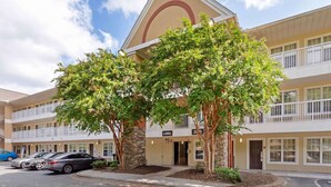 A multi-story hotel with a lobby entrance, parking area, and a clear sky. - Extended Stay America Suites Durham University (Durham)