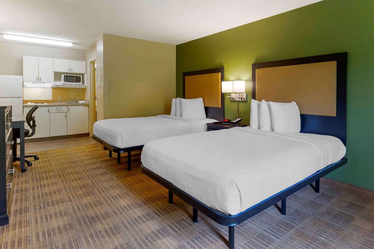 A hotel room with two beds, a kitchenette, and a green accent wall.