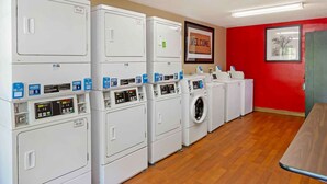 A laundry room with multiple washing machines and dryers, a welcome sign, and a framed picture on the wall. - Extended Stay America Suites Durham University (Durham)