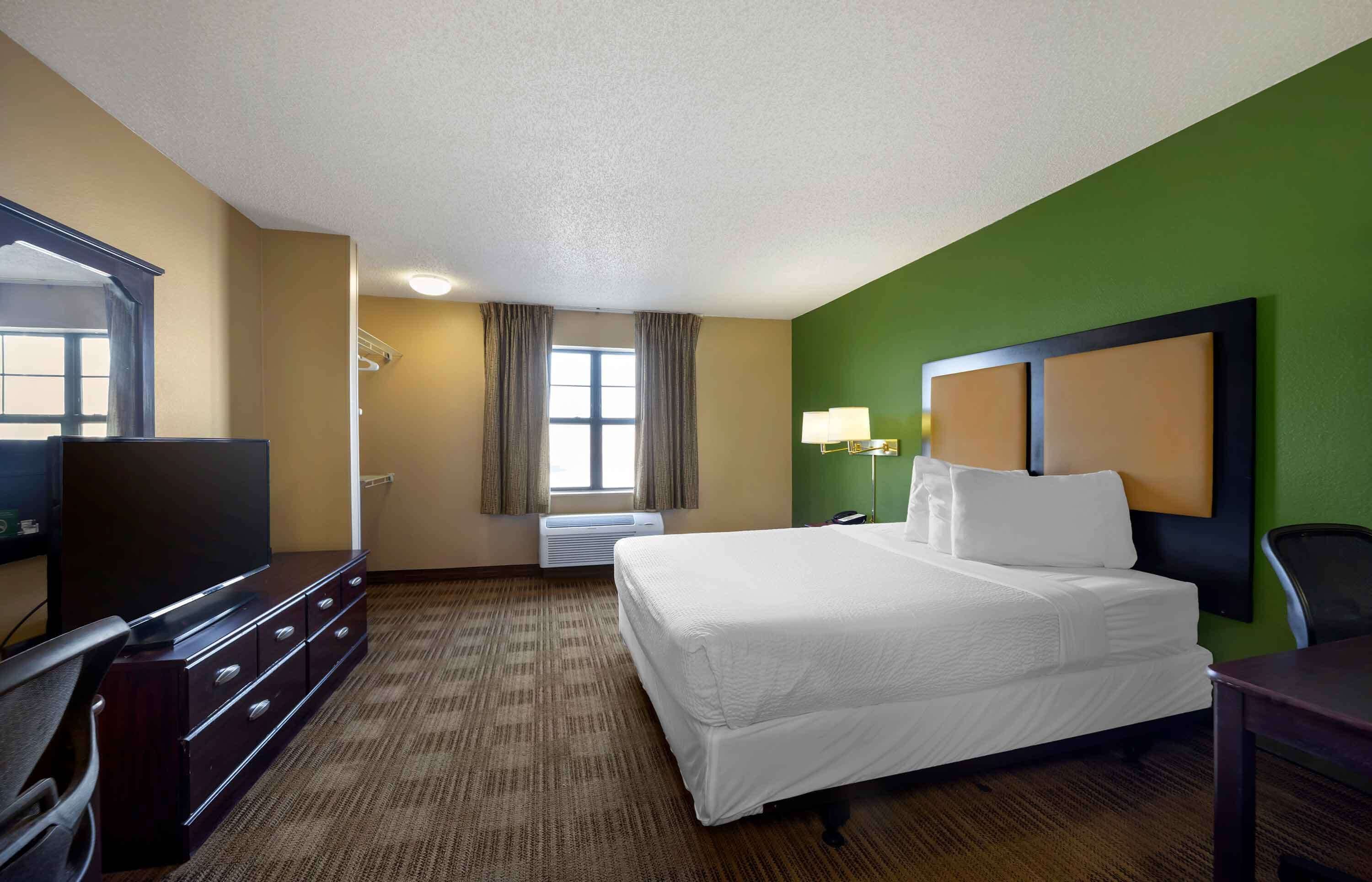 A hotel room with a bed, a TV, a dresser, and a window with curtains.