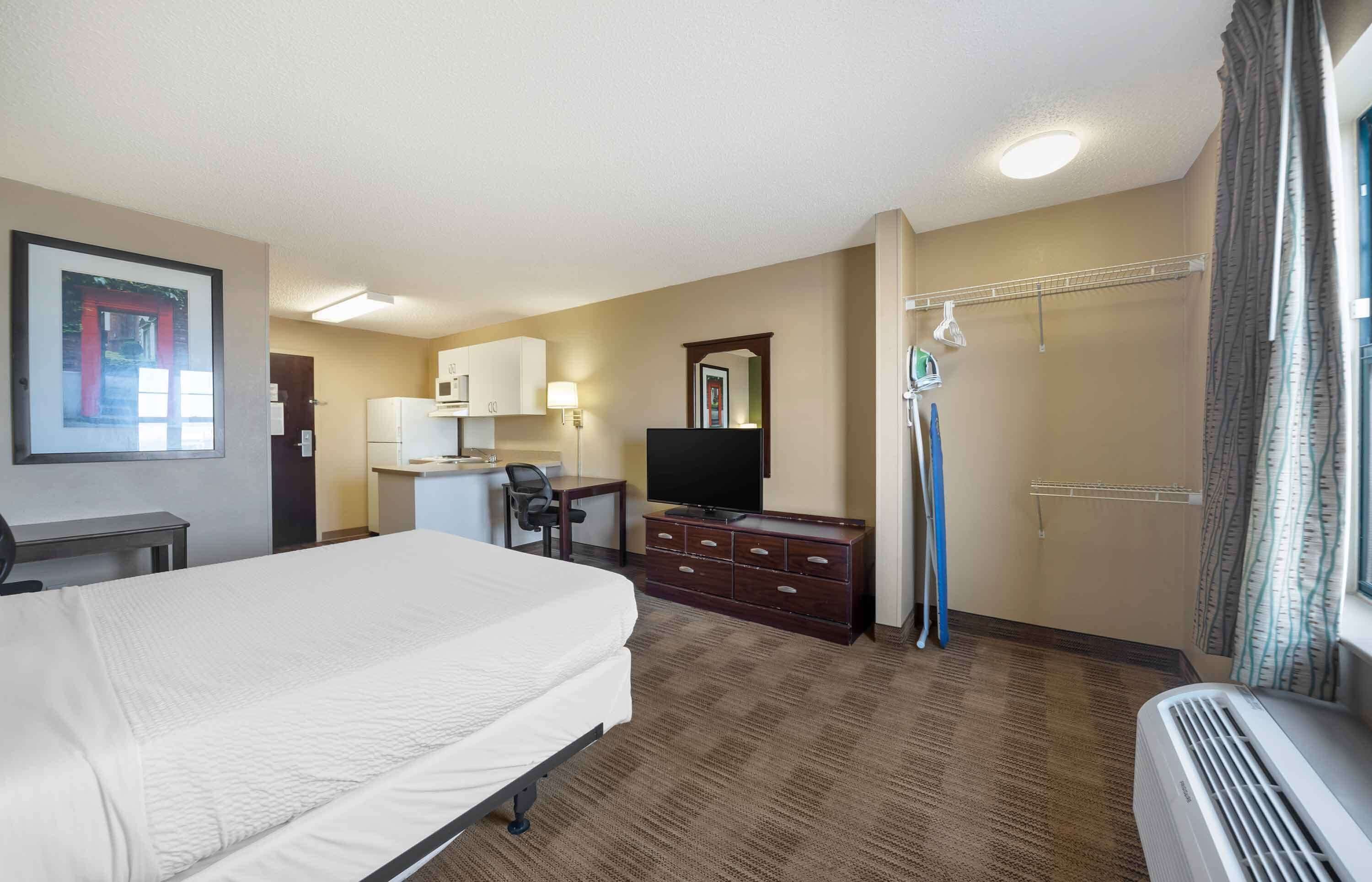 A hotel room with a bed, a desk with a chair, a television, a wardrobe, and a bathroom with a shower curtain.