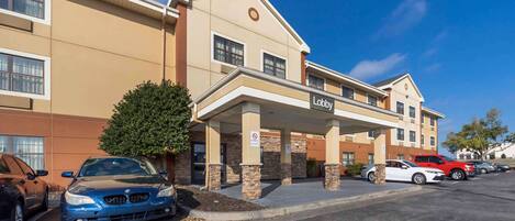 Un hotel con un letrero que dice 'Lobby', un estacionamiento y una fachada de tonos beige y marrón.