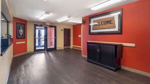 A hotel lobby with a red wall, a welcome sign, a black cabinet, and a door with an exit sign. - Suburban Studios (Oklahoma City)