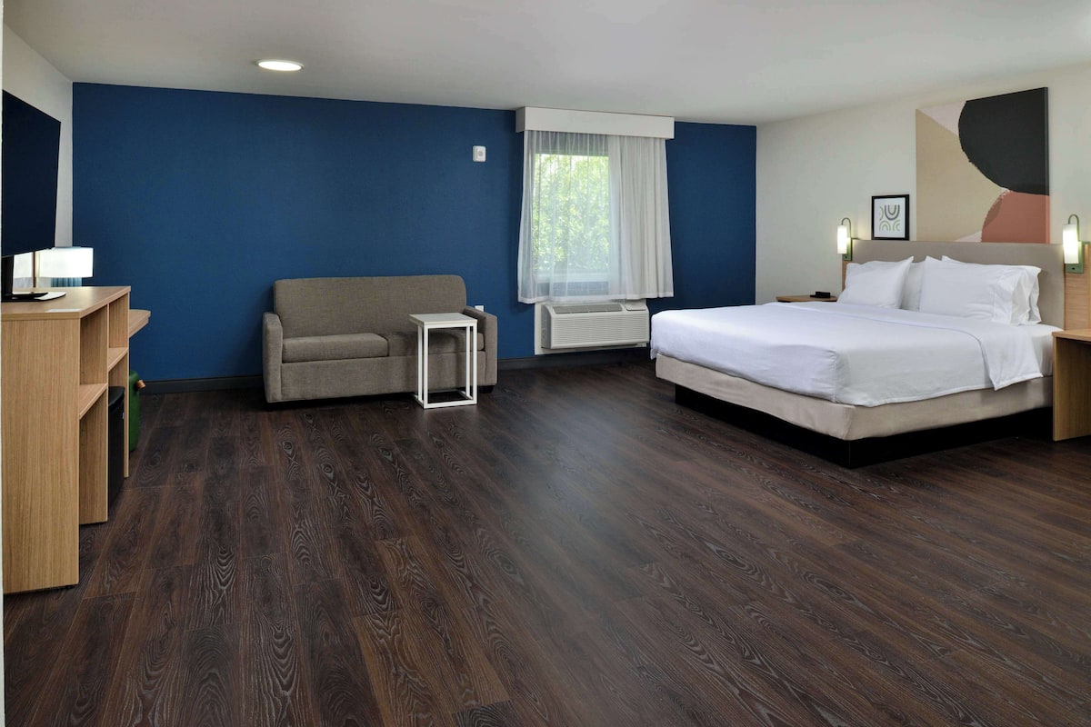 A hotel room with a large bed, a sofa, a desk, and a window with curtains.