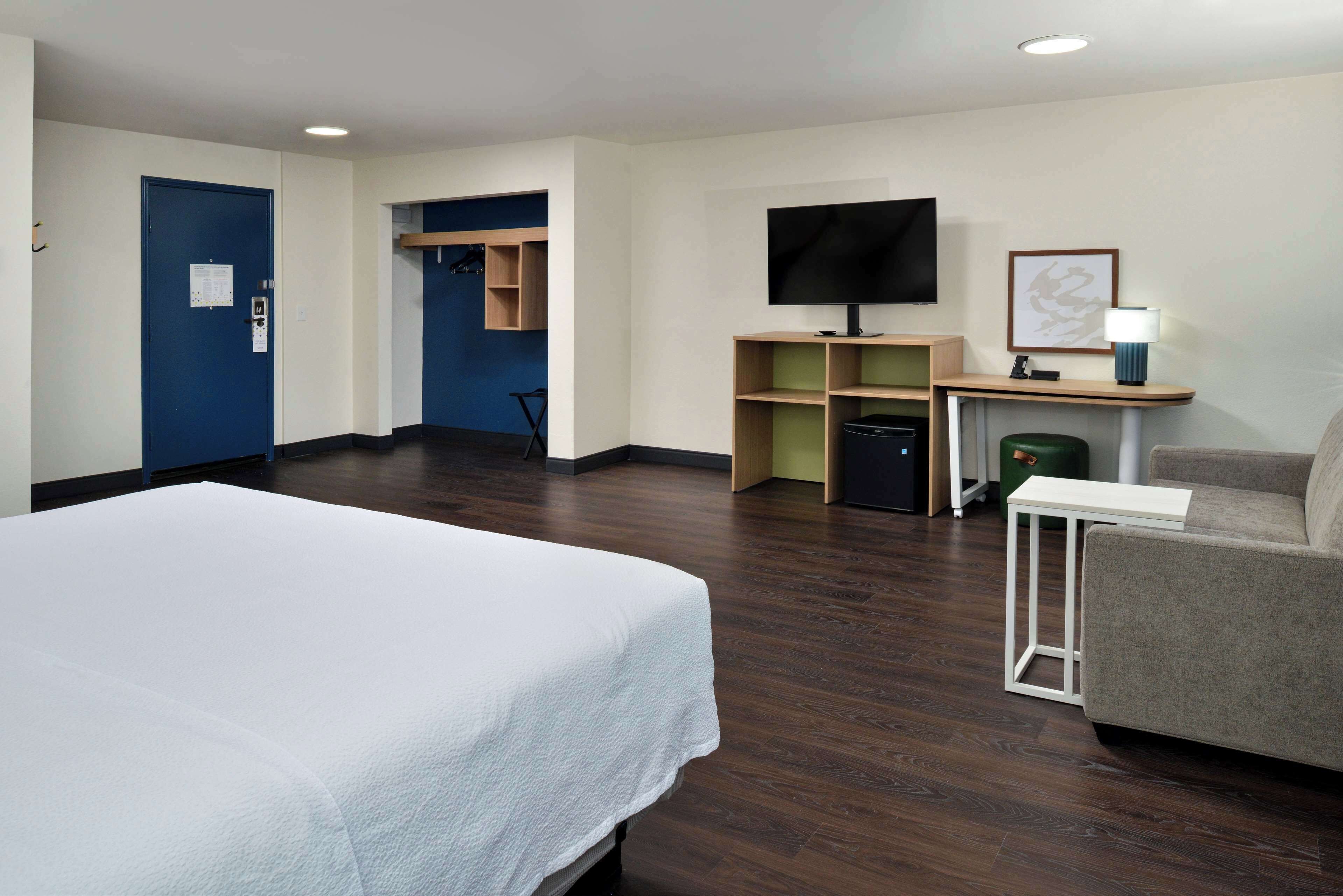 A hotel room with a bed, a desk with a TV, a chair, and a small table.