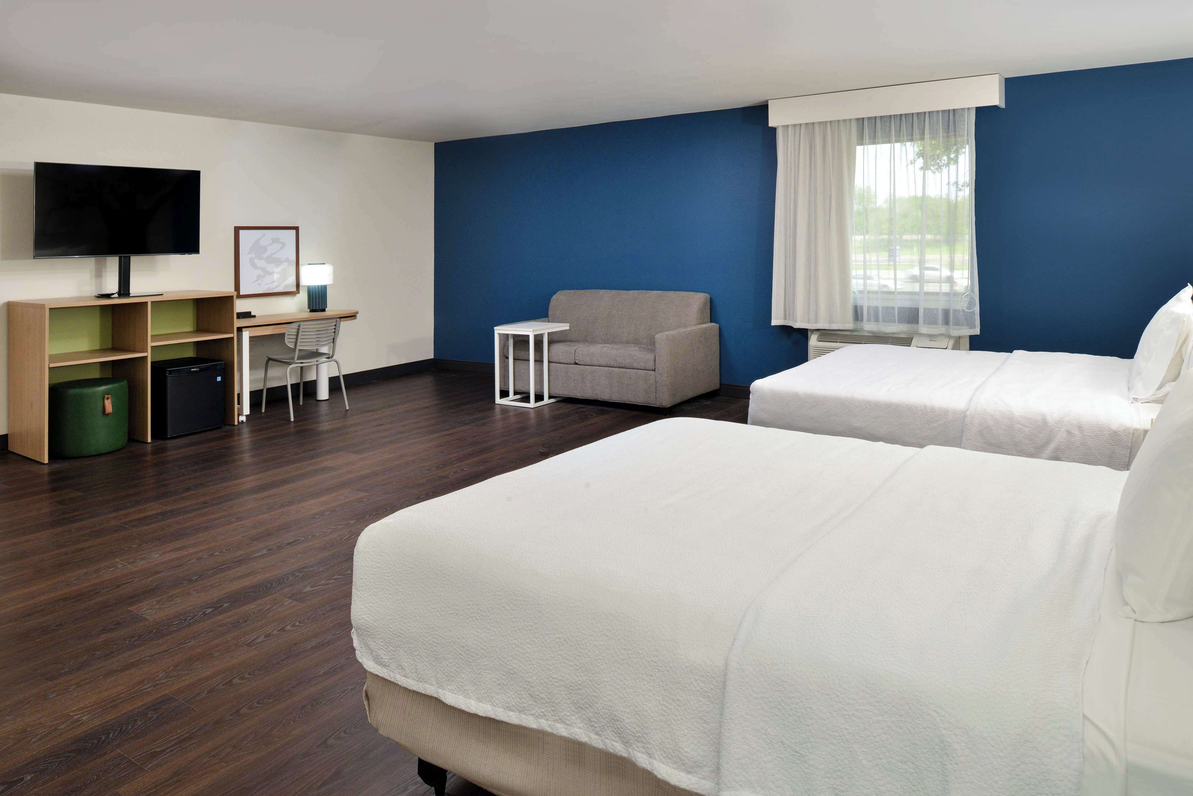 A hotel room with two beds, a desk with a computer, a TV, and a chair.