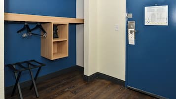 Une pièce avec une porte bleue, une étagère en bois avec des cintres, une petite armoire en bois et une table pliante en métal.