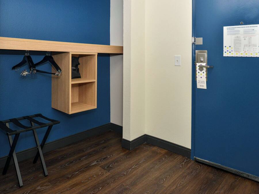 Une pièce avec une porte bleue, une étagère en bois avec des cintres, une petite armoire en bois et une table pliante en métal.