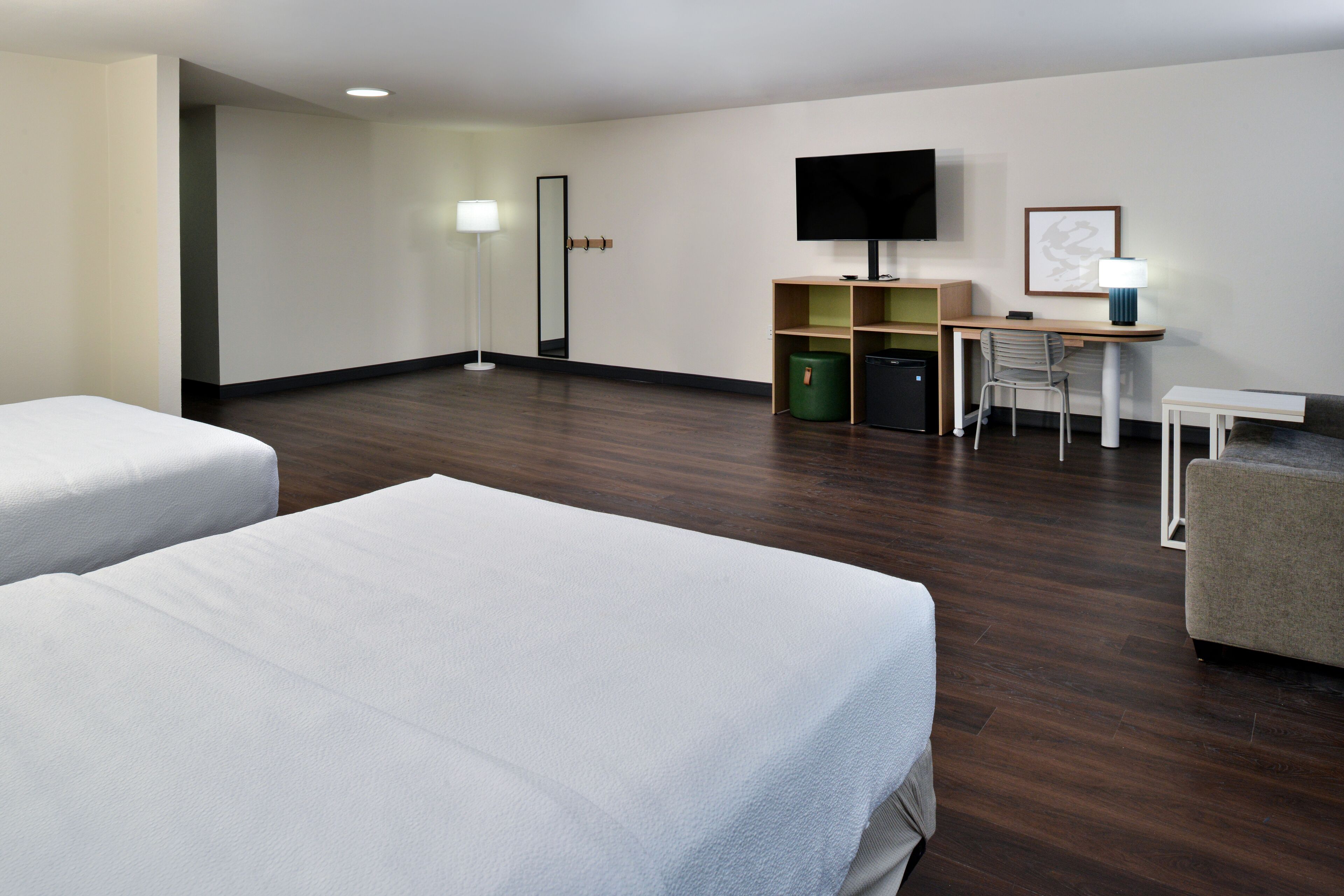 A hotel room with two beds, a desk, a chair, a television, and a lamp.