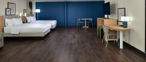 A hotel room with two beds, a desk, a chair, and a table.