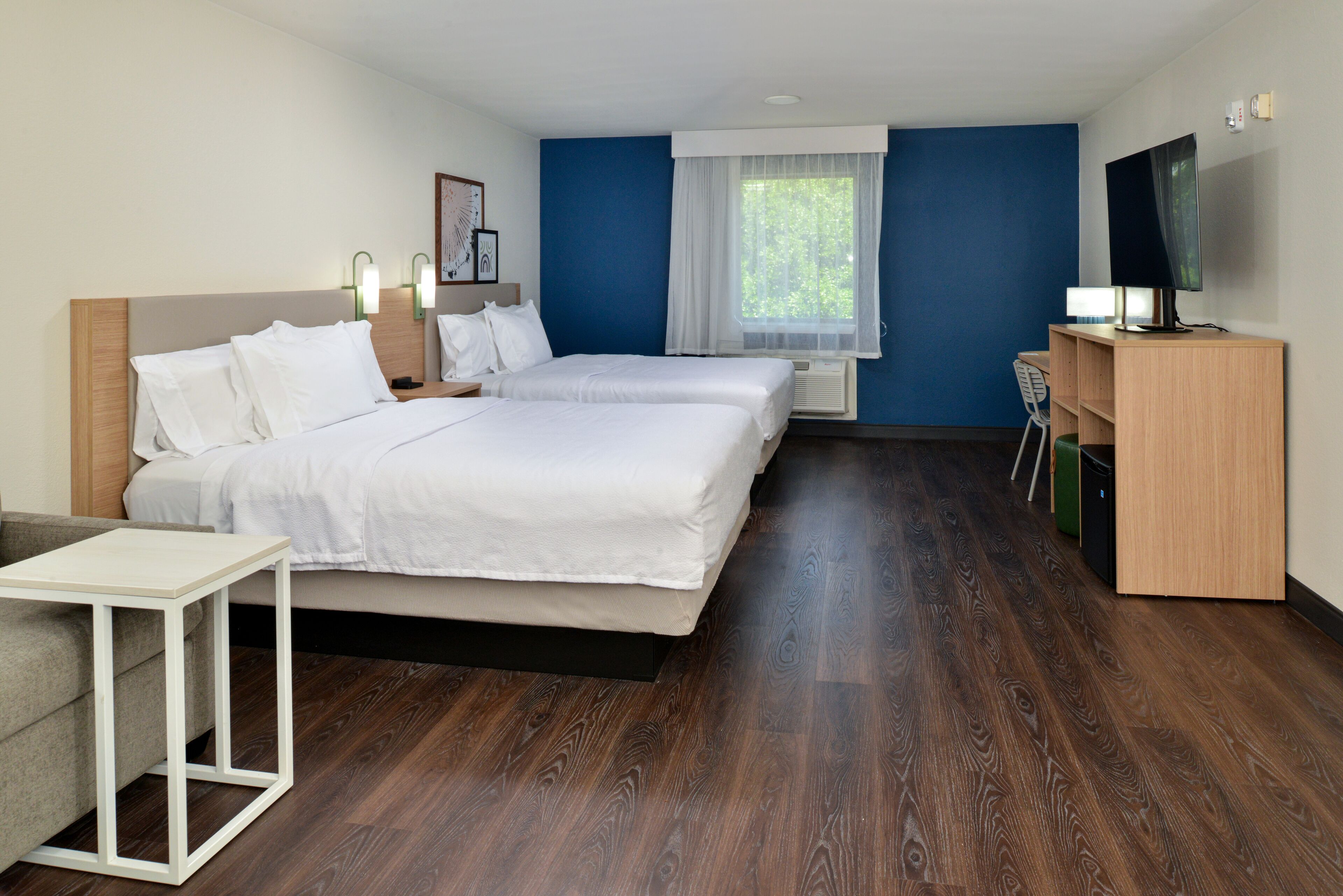 A hotel room with two beds, a TV, a desk, and a window with curtains.