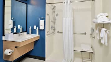 A bathroom with a sink, mirror, towel rack, shower with a glass door, and a small table.
