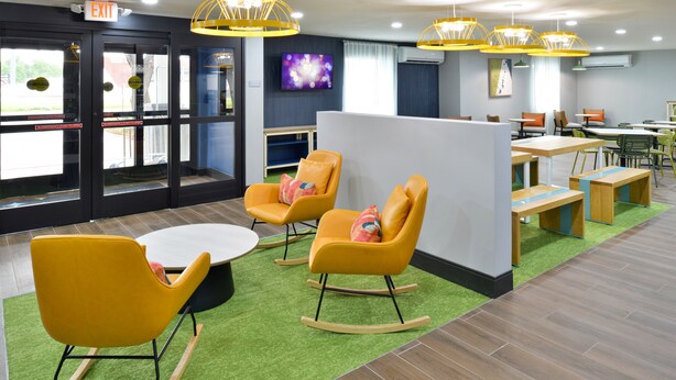 A modern interior with yellow rocking chairs, a white table, and green artificial grass flooring. - Spark by Hilton Dallas Medical District Love Field (Dallas)