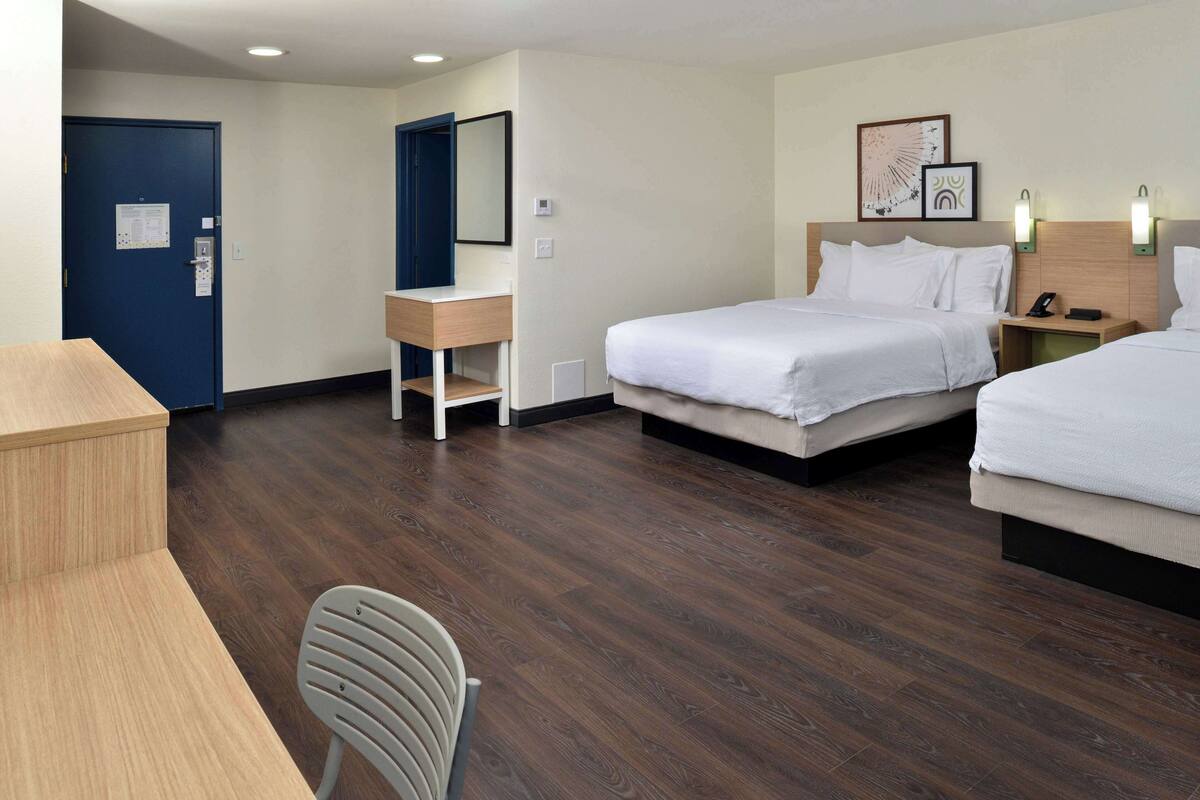 A hotel room with two beds, a desk, a chair, a dresser, and a mirror.