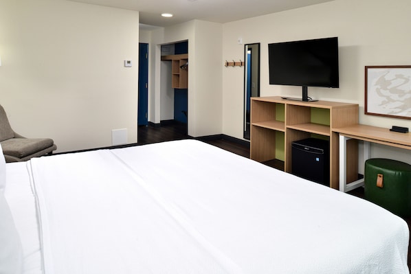 Habitación de hotel con cama, televisor, escritorio, silla, armario y basurero.