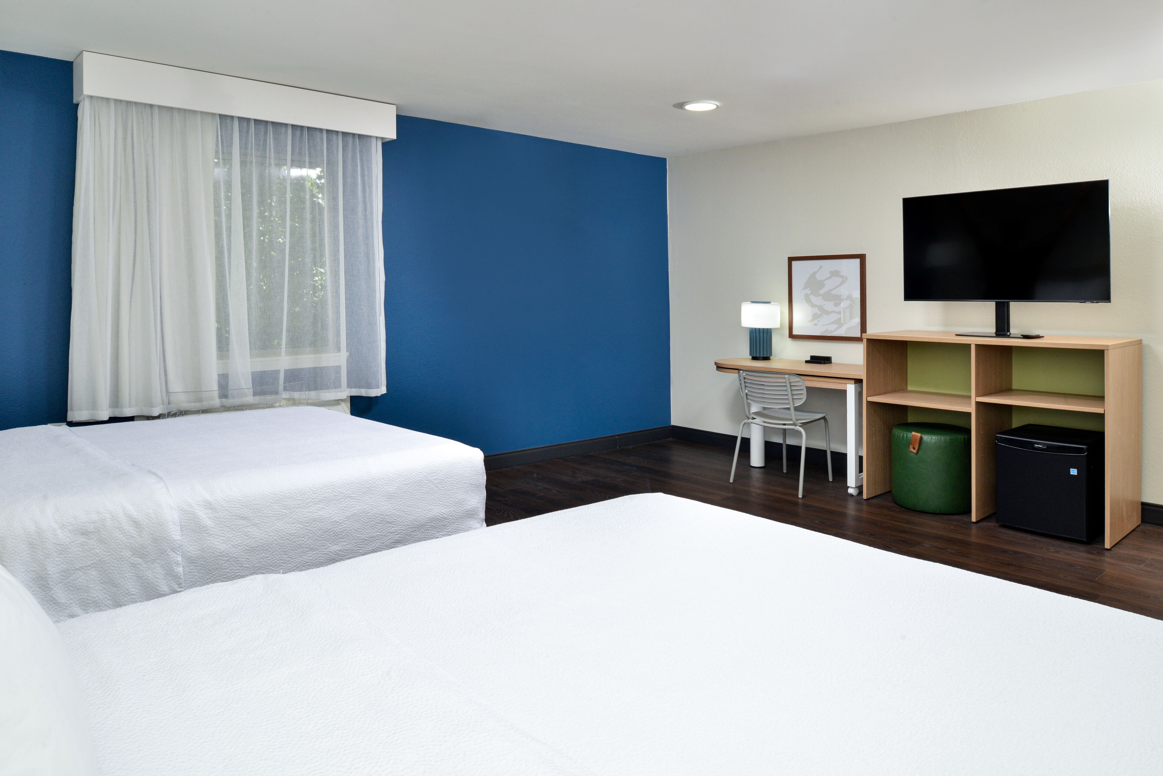 Una habitación de hotel con dos camas, un escritorio con silla, televisor y armarios.