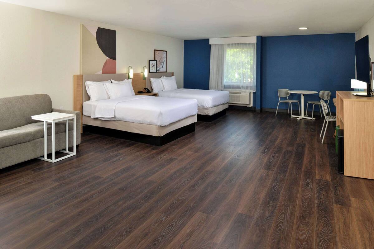 A hotel room with two beds, a sofa, a small table, a desk, and a chair.