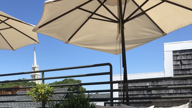 Eine Dachterrasse mit Gartenmöbeln, darunter ein Tisch mit Obstschale, umgeben von großen Sonnenschirmen.
