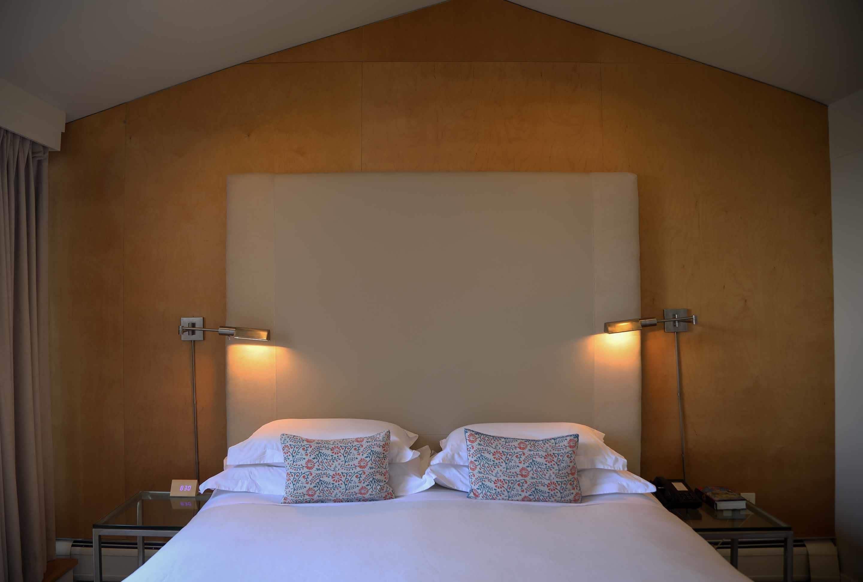 A hotel room with a large bed, two bedside tables, a nightstand, and a wall-mounted lamp.