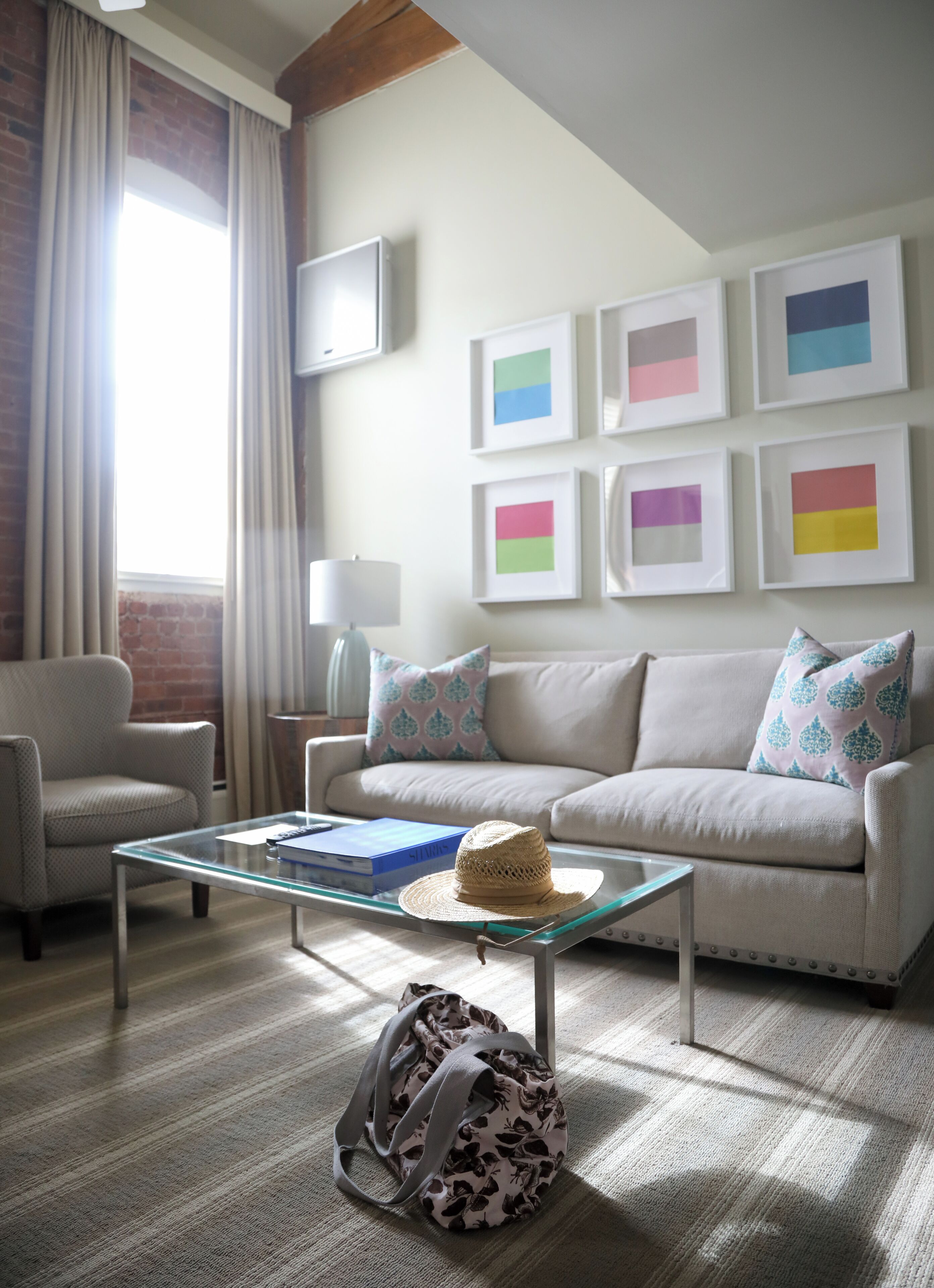 A living room with a sofa, a glass coffee table, a chair, a lamp, and a wall with framed artwork.