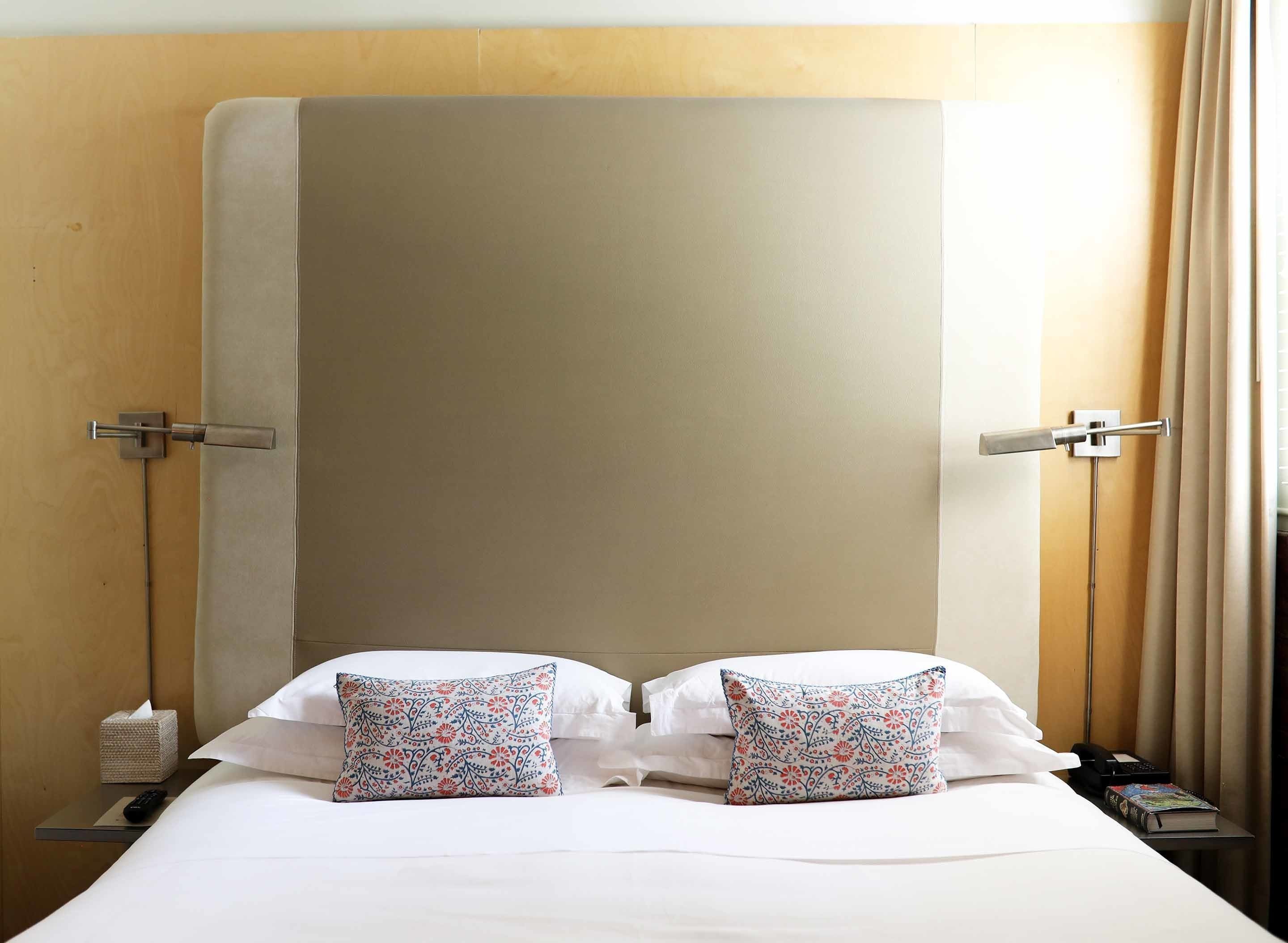 A hotel room with a large bed, two pillows, a bedside table with a phone and a book, and a nightstand with a tissue box and remote control.