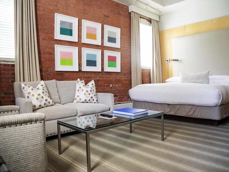 A hotel room with a sofa, a bed, a glass coffee table, and a wall with framed artwork.