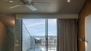 Ein Hotelzimmer mit einem großen Bett, einem Deckenventilator, einer Glastür, die zu einem Sitzbereich mit Stühlen und einem Tisch im Freien führt.