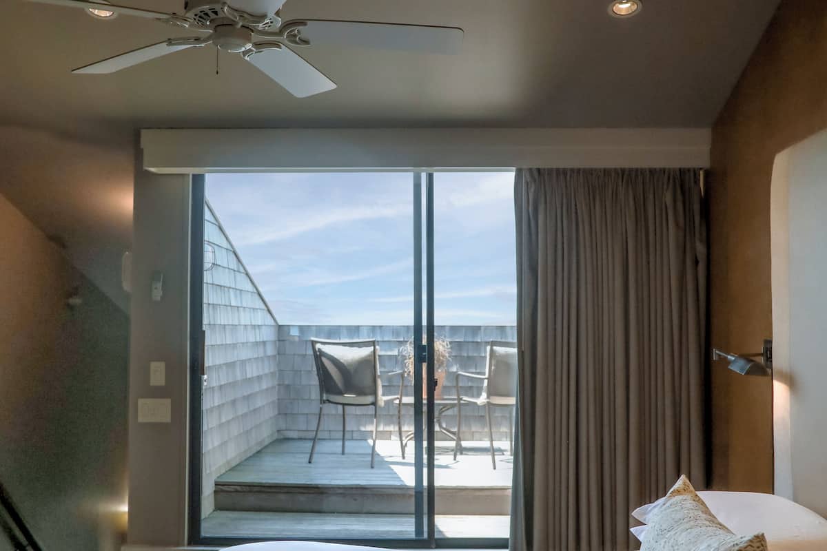 A hotel room with a large bed, a ceiling fan, a sliding glass door leading to an outdoor seating area with chairs and a table.