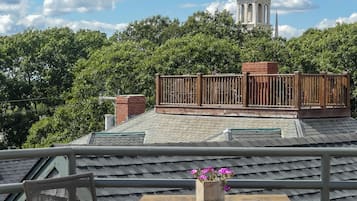 A balcony with a table and chair, a flower pot, and a view of a church spire.