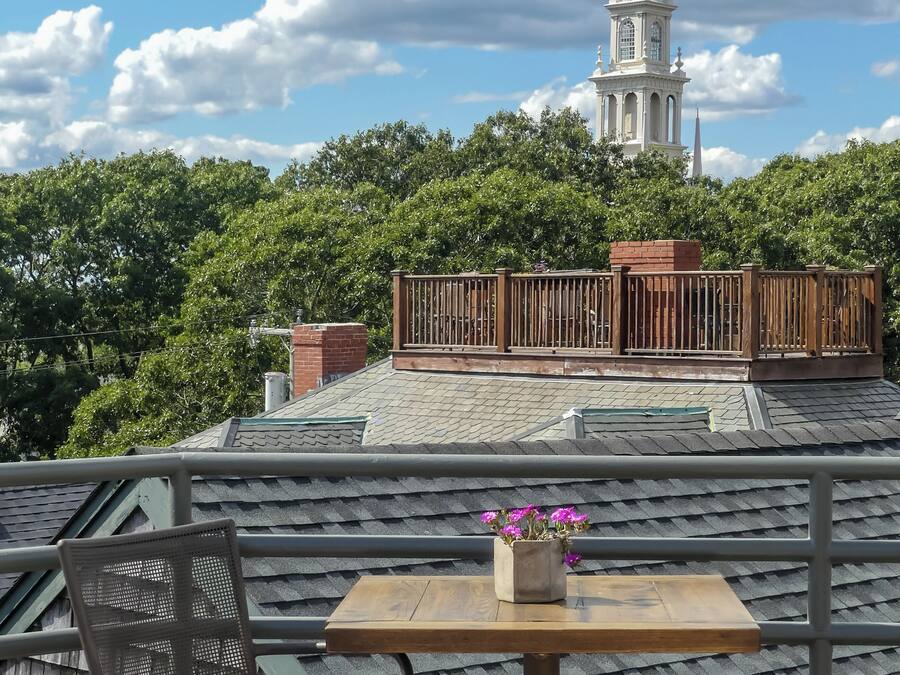 A balcony with a table and chair, a flower pot, and a view of a church spire.