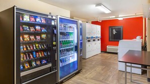 A hotel lobby with vending machines selling snacks and drinks, a white reception desk, and a red accent wall. - Extended Stay America Suites Wilmington New Centre Drive (Wilmington)