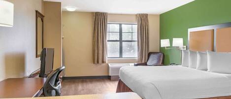 A hotel room with a bed, a desk, a chair, a TV, a window with curtains, and a green accent wall.
