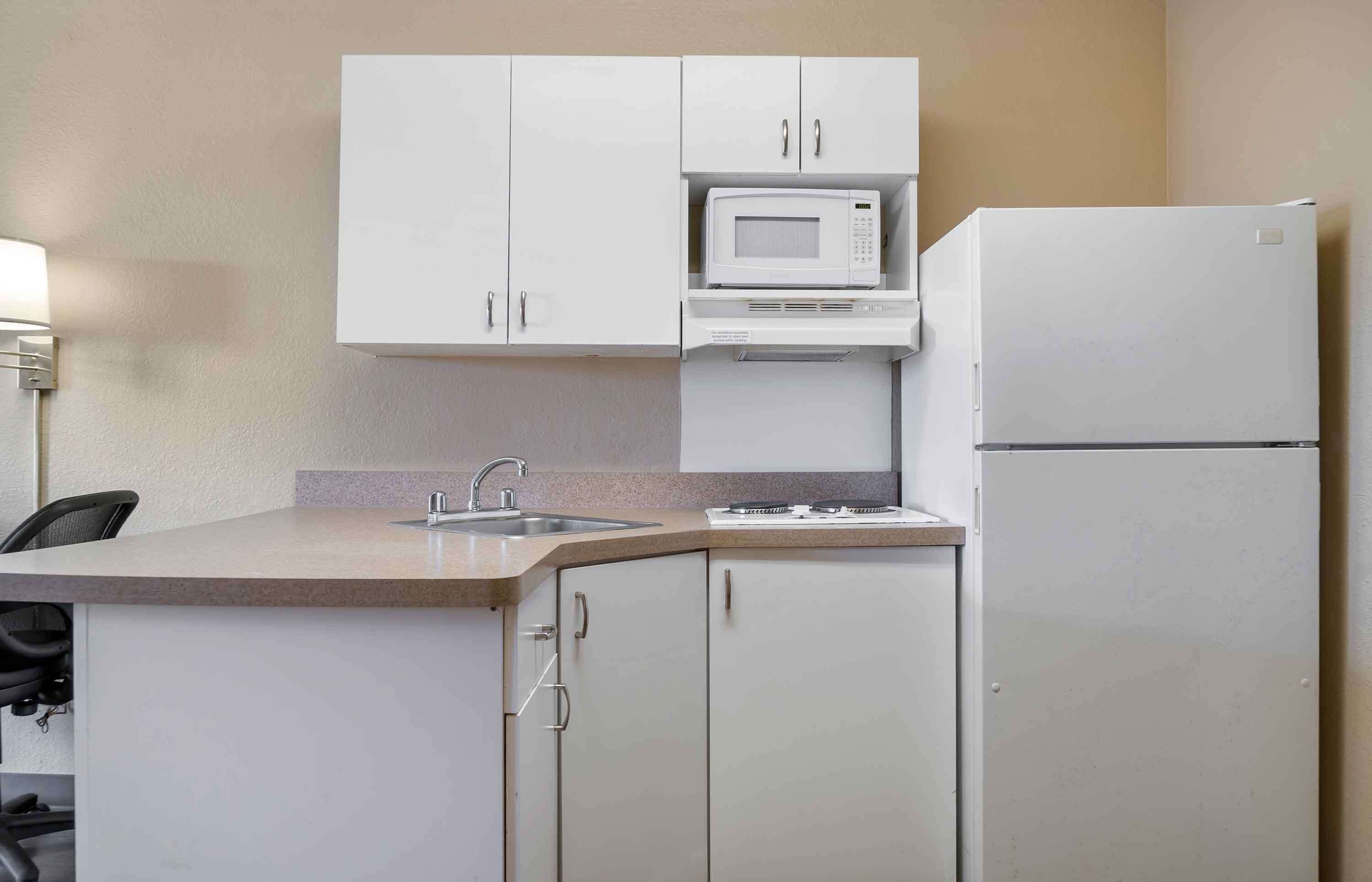 A compact kitchen with white cabinets, a microwave, a refrigerator, and a sink.
