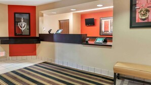 Zona de recepción de hotel con pared de acento roja, mostrador de recepción, un banco y una obra de arte enmarcada en la pared.