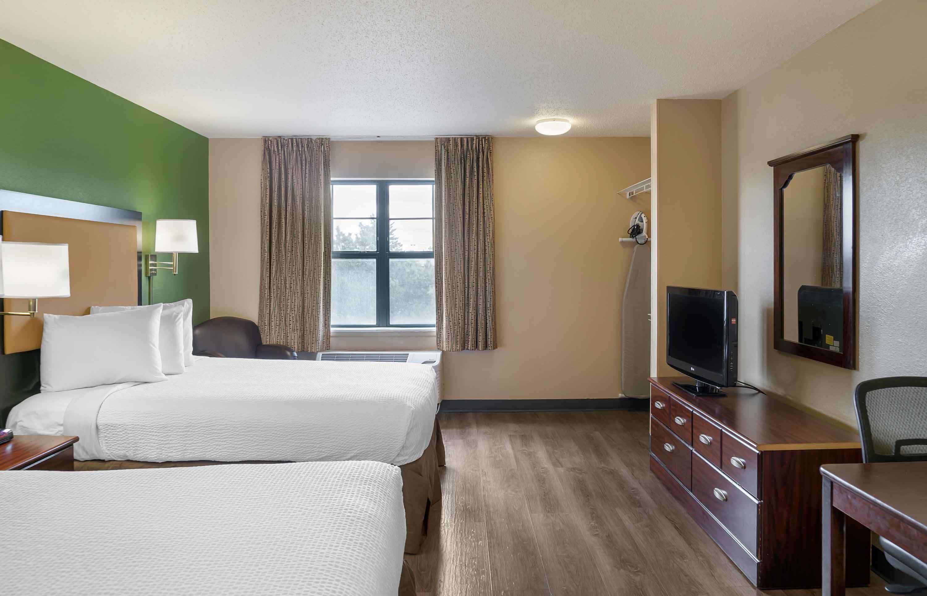 A hotel room with two beds, a desk, a television, and a mirror.