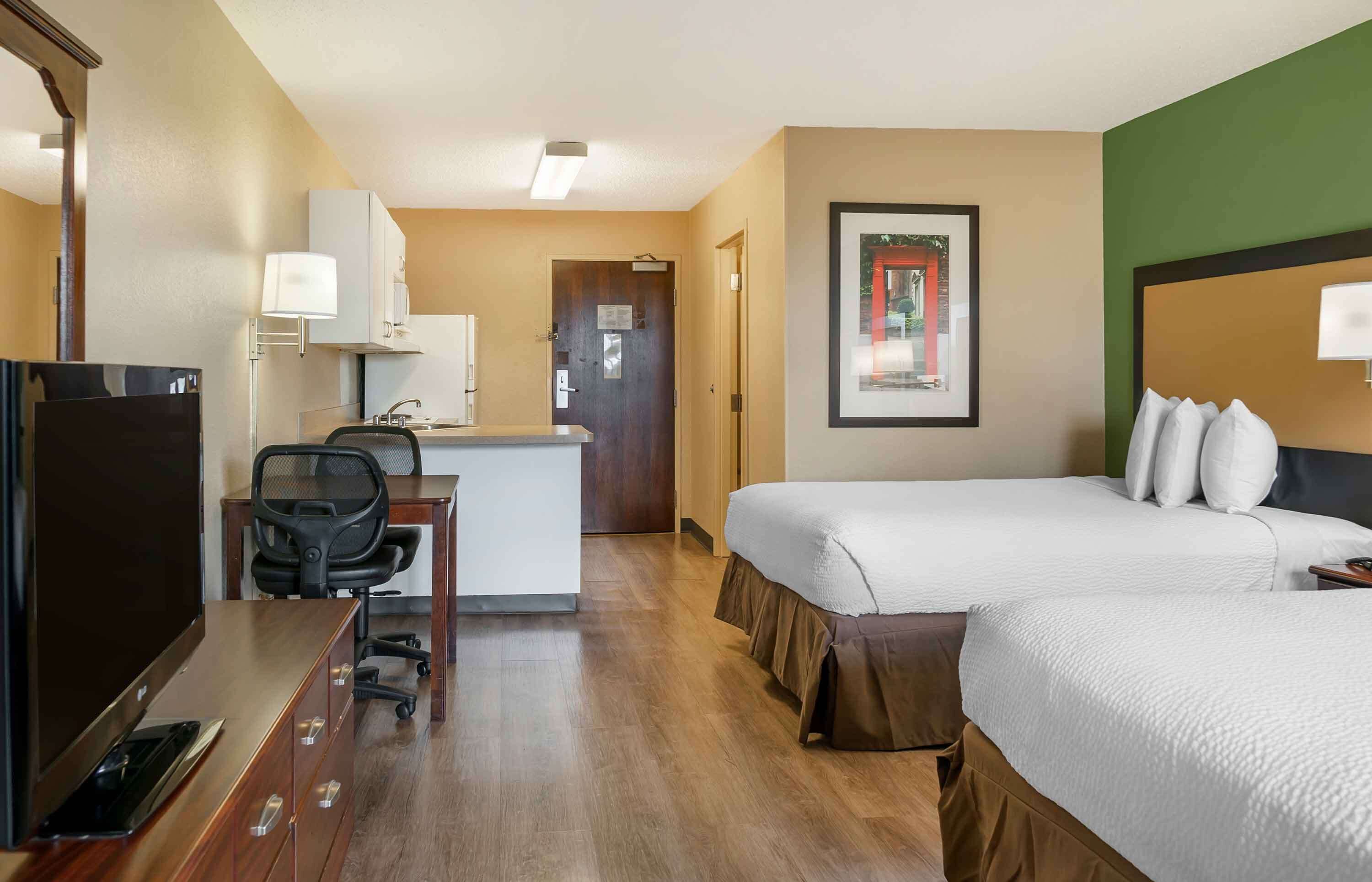 A hotel room with a desk, two beds, a TV, and a framed picture on the wall.