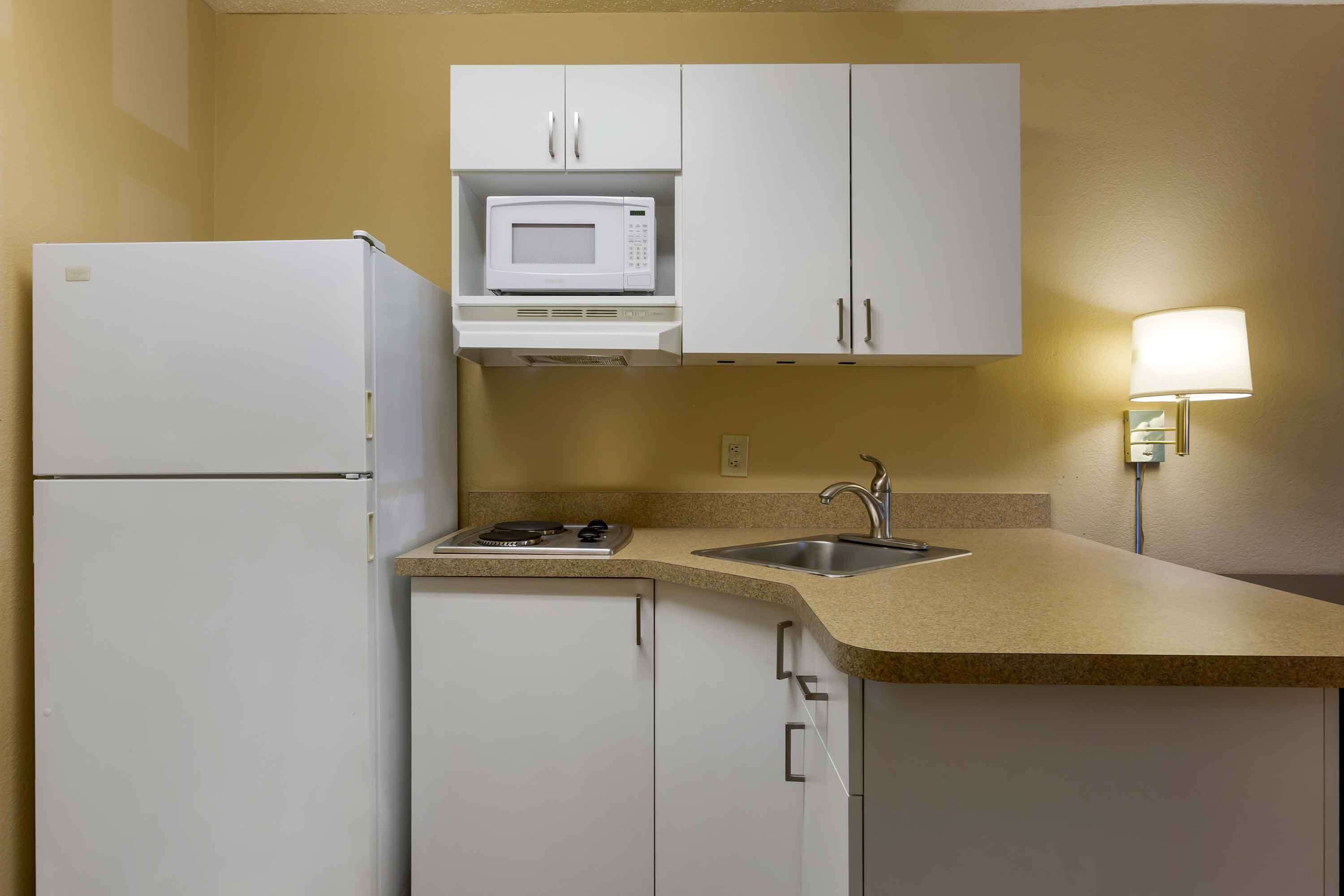 A compact kitchen with white cabinets, a microwave, a refrigerator, a sink, and a countertop.