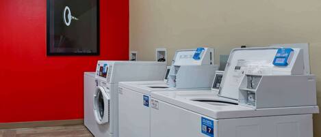A laundry room with three white washers and dryers, a red wall, and a ceiling light fixture.