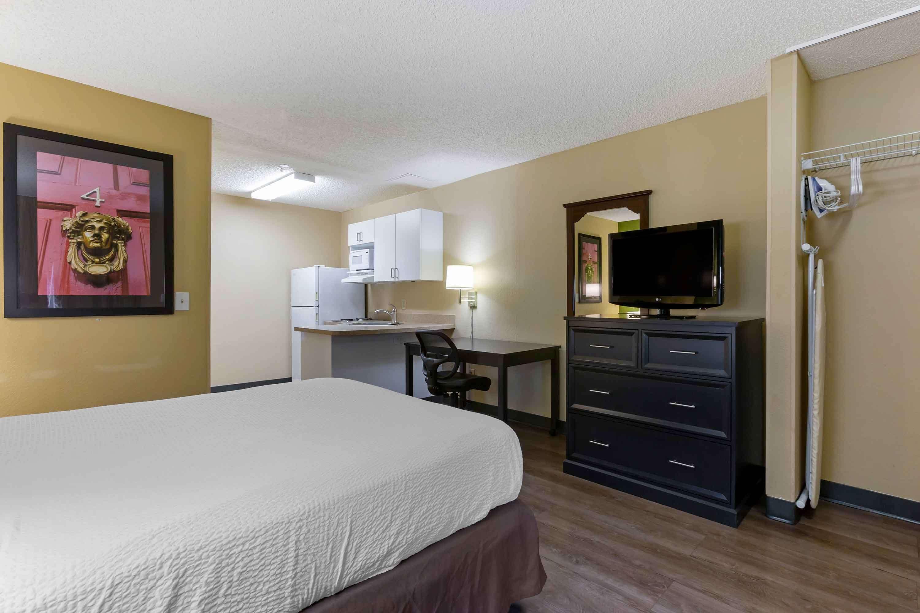 A hotel room with a bed, a desk with a computer, a television, and a wardrobe.