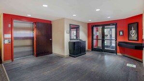 Un hall d’hôtel avec un plancher en bois, des murs rouges, un meuble noir et une porte en verre.