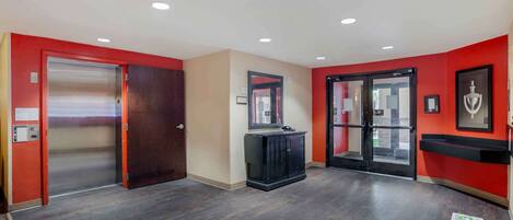 Un vestíbulo de hotel con piso de madera, paredes rojas, un mueble negro y una puerta de vidrio.