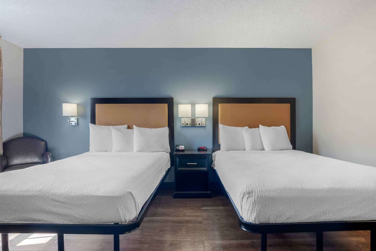 Une chambre d’hôtel avec deux lits simples, une table de chevet avec une lampe et une chaise.