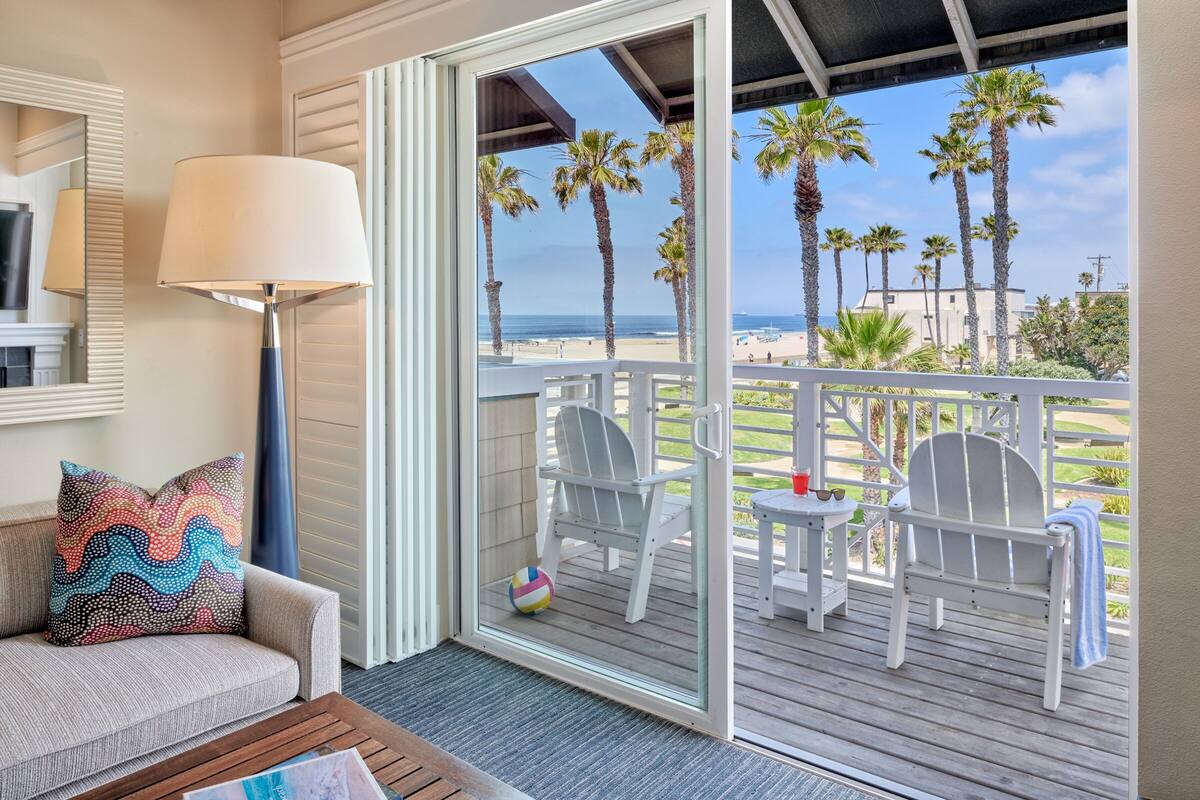 Un balcon avec vue sur la plage, des chaises blanches et un ballon de plage aux couleurs vives.