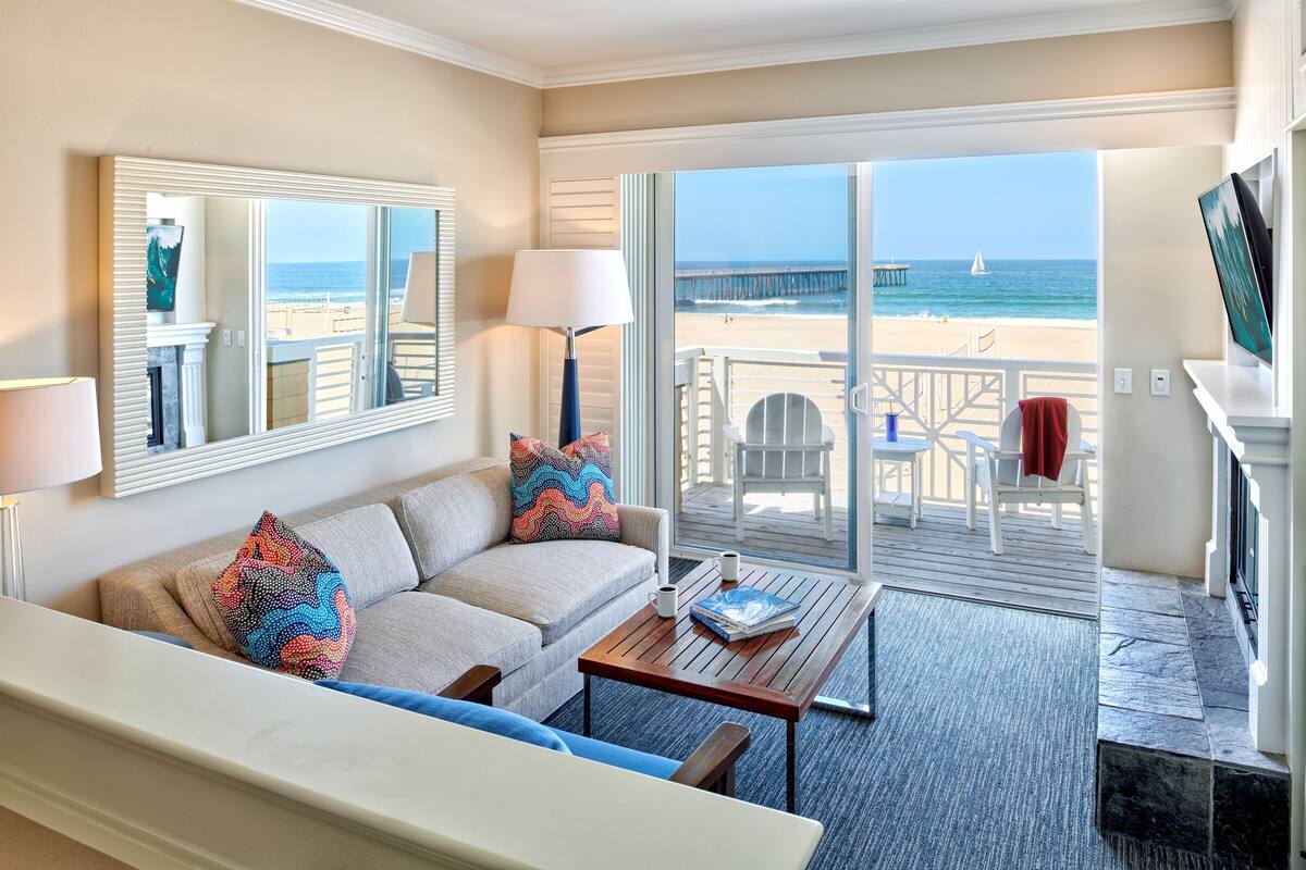 Une chambre d’hôtel équipée d’un canapé, d’une table basse, d’une télévision et d’un balcon offrant une vue sur la plage et l’océan.