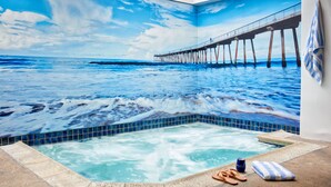 Una habitación con un gran mural de un muelle que se adentra en el océano, un jacuzzi y un perchero.