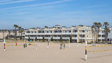 A beach volleyball court with a net, surrounded by a hotel with balconies and palm trees.