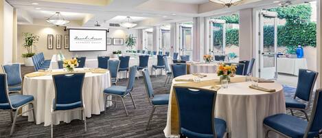 A conference room with multiple tables and chairs, large windows, and a projector screen.