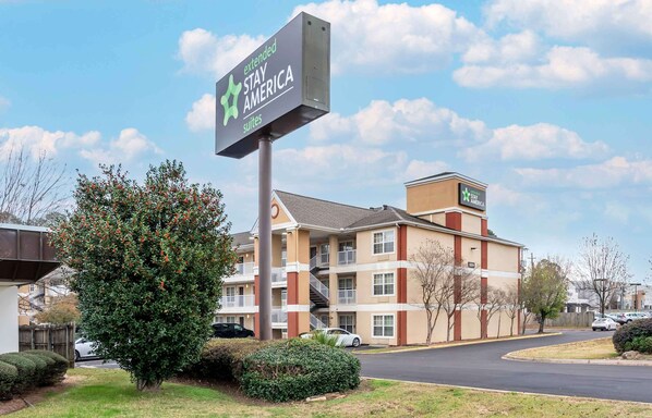 Un hotel Stay America con letrero, un edificio de varios pisos y un estacionamiento.