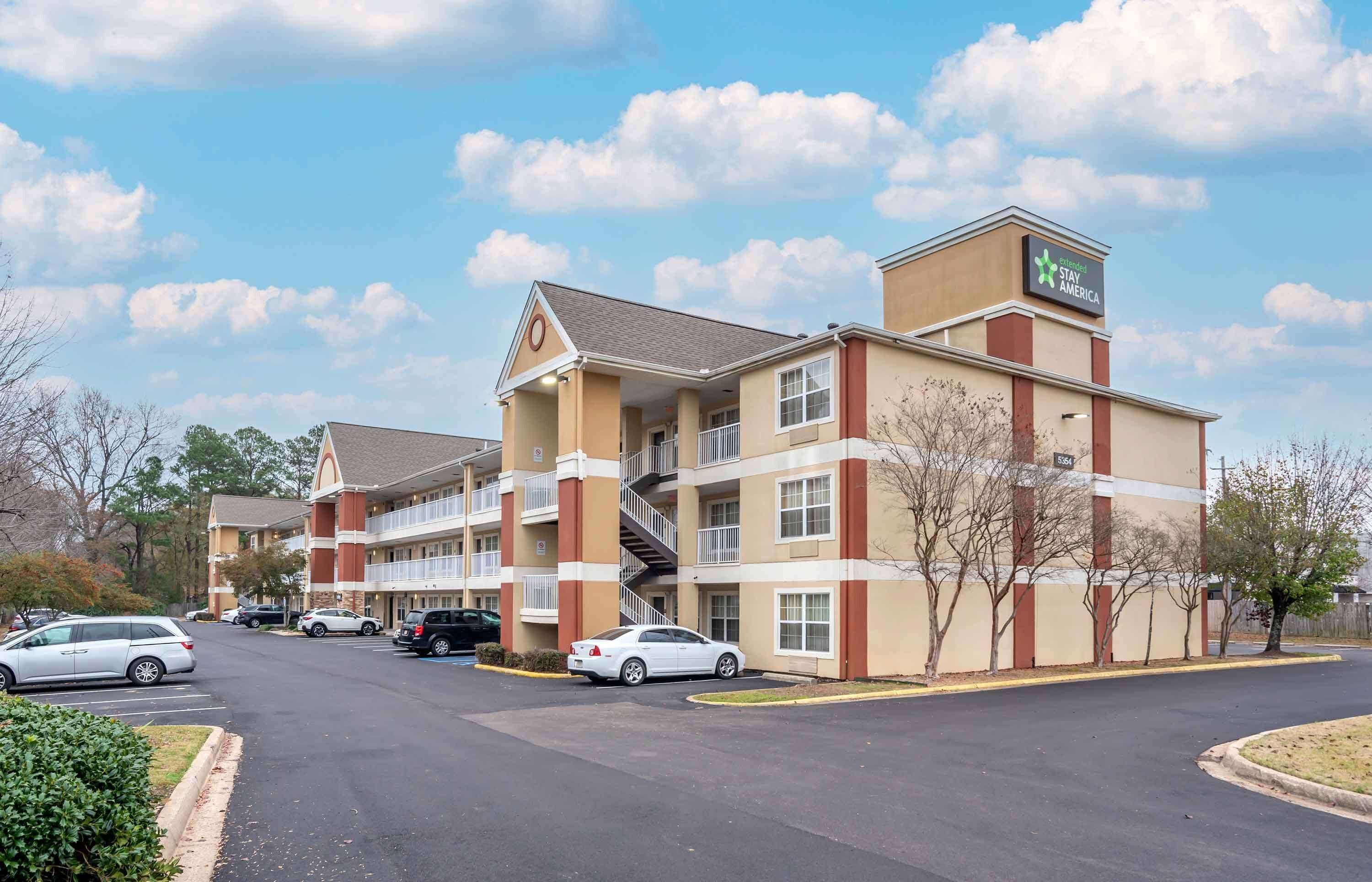 A Stay America hotel with a two-story structure, multiple balconies, and a parking lot with several cars.