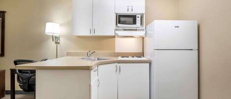 A compact kitchen with white cabinets, a microwave, a refrigerator, a sink, and a small island with a chair.